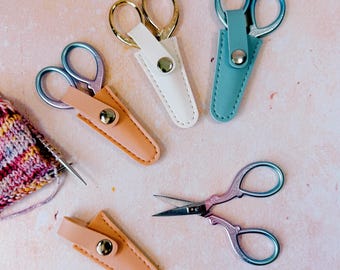 Tijeras pequeñas de bordar con funda de seguridad para labores de hilo y costura, color rosa, azul y crema.