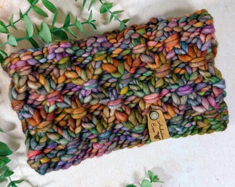 May include: A chunky knit headband in a mix of colors including orange, green, purple, and brown. The headband has a tag that reads "Artisan Eve". The item is made of thick, textured yarn.