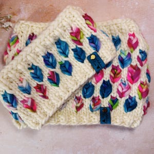 May include: A white knitted headband and matching scarf with a colorful leaf pattern. The headband and scarf have leather tags with the text "A Little Something" on them.