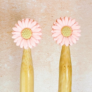 May include: Two wooden knitting needles with pink daisy flower-shaped tops. The needles are made of natural bamboo.