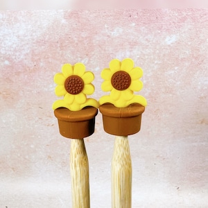 May include: Two brown ceramic flower pots with yellow sunflower tops on wooden sticks.