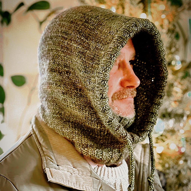 May include: A knitted hood in shades of olive green and brown, with a drawstring closure. The hood is made of a textured yarn and is worn over a jacket. The overall style is casual and warm, suitable for cold weather.