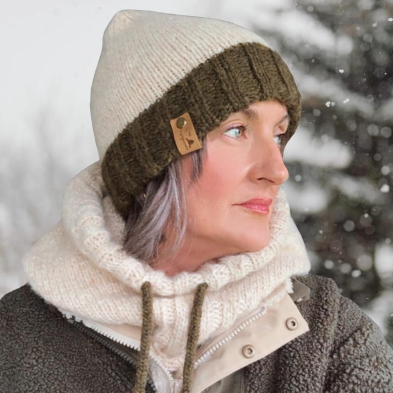 May include: A knitted winter hat with a cream-colored crown and an olive green brim. A small leather tag is sewn on the side. The hat is worn with a cream-colored neck warmer and a green jacket.
