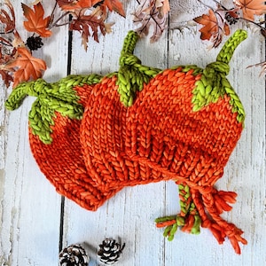 Peut inclure: Deux bonnets en tricot en forme de citrouille avec des tiges vertes et des corps orange. Les bonnets ont de longues franges et sont faits avec un fil épais.