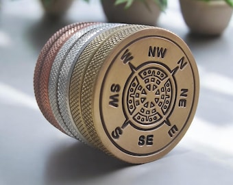 May include: A set of four stacked metal stampers with a compass rose design. The stampers are made of different metals, including copper, silver, and gold. The compass rose features the cardinal directions: N, S, E, W, NE, NW, SE, and SW.