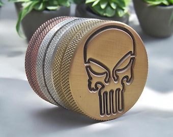May include: A multi-layered metal stamp with a skull design. The stamp is made of copper, silver, and gold metal. The skull is engraved in the top layer of the stamp.