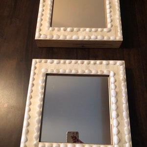 May include: Two white framed mirrors with a shell design. The mirrors are square and have a simple, clean design.