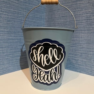 May include: A light blue metal bucket with a wooden handle and a black and white sticker that says "shell yeah!"