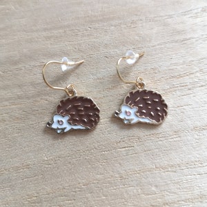 Peut inclure: Une paire de boucles d'oreilles dorées avec un motif de hérisson en émail brun et blanc.