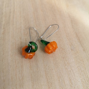 Peut inclure: Une paire de boucles d'oreilles pendantes avec de petites citrouilles en verre orange et des tiges vertes. Les boucles d'oreilles sont faites de fil d'argent.