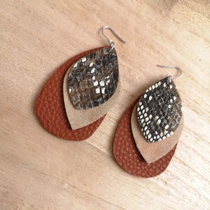 Peut inclure: Une paire de boucles d'oreilles en cuir superposées avec un motif de peau de serpent brun, beige et noir. Les boucles d'oreilles sont en forme de goutte et ont des crochets argentés.
