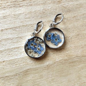 Peut inclure: Une paire de boucles d'oreilles en argent avec des fleurs bleues de myosotis pressées dans de la résine transparente.