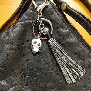 May include: A black leather handbag with a silver key chain attached. The key chain features a small panda charm and a black and white tassel.