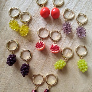 Peut inclure: Un ensemble de 10 paires de boucles d'oreilles créoles dorées avec différents pendentifs en forme de fruits. Les pendentifs comprennent des grenades rouges, des raisins verts, des raisins violets et des grappes de baies jaunes et violettes.