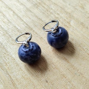 May include: A pair of silver hoop earrings with a dark blue, marbled, round charm attached to each hoop.