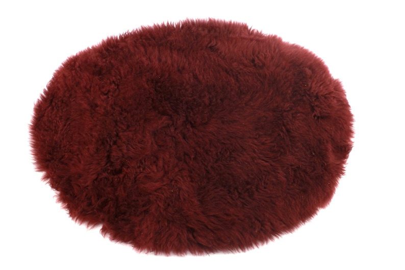 May include: A burgundy sheepskin rug with a soft, fluffy texture. The rug is oval shaped and perfect for adding warmth and comfort to any room.