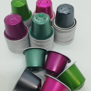May include: A collection of colourful coffee pods in green, pink, and grey. The pods are stacked in piles and some are scattered on a white surface.