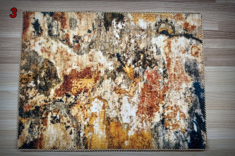 May include: Rectangular rug with an abstract design in shades of brown, yellow, and blue. The rug has a textured appearance with a rope-like border. The number "3" is visible in the upper left corner.
