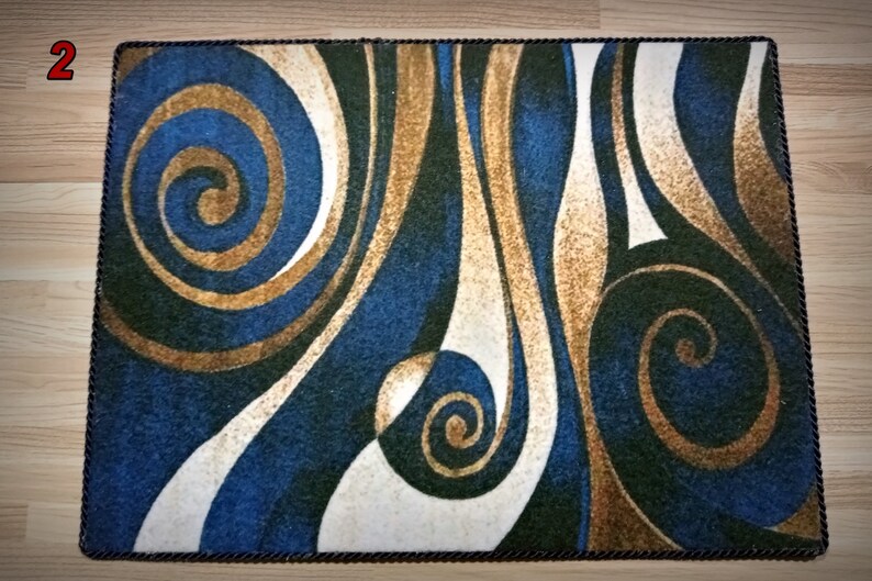 Peut inclure: Tapis rectangulaire avec un motif abstrait tourbillonnant dans les tons de bleu, or, blanc et vert. Le tapis a une bordure marron fonc&eacute; et un motif de lignes courbes et de spirales. Id&eacute;al pour une utilisation en int&eacute;rieur.