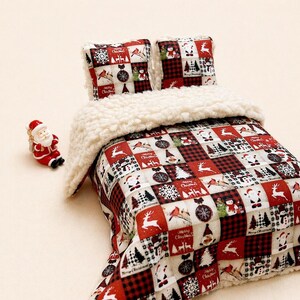 Può includere: Un set di biancheria da letto a tema natalizio con un design patchwork rosso e bianco. I quadrati mostrano immagini festive come renne, Babbo Natale e fiocchi di neve. Il set include una coperta con un bordo soffice color crema e due cuscini abbinati. Una piccola statuina di Babbo Natale è accanto.