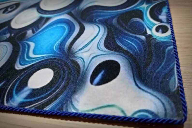 Peut inclure: Gros plan sur un tapis &agrave; motifs bleus et blancs avec une bordure en corde bleu fonc&eacute;. Le motif pr&eacute;sente des motifs tourbillonnants dans les tons de bleu, de blanc et de noir, cr&eacute;ant un aspect fluide et abstrait. Les bords du tapis sont soigneusement finis.