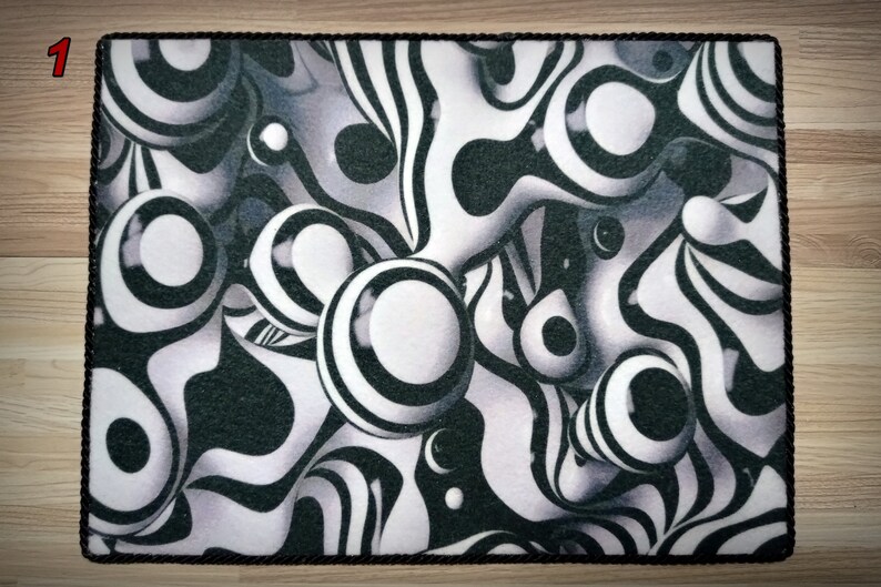 Peut inclure: Un tapis rectangulaire avec une bordure en corde noire. Le tapis pr&eacute;sente un motif abstrait noir, blanc et gris avec des formes sph&eacute;riques et ondul&eacute;es. Le design cr&eacute;e un effet 3D, avec les formes semblant flotter.