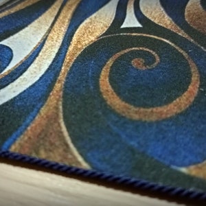 Peut inclure: Un tapis rectangulaire avec un motif tourbillonnant dans les tons de bleu, or, blanc et noir. Le tapis a une bordure en corde bleu fonc&eacute;. Le design pr&eacute;sente des lignes courbes et des formes en spirale.
