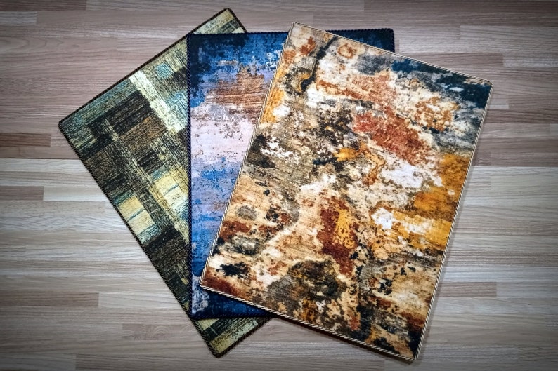 May include: Three rectangular rugs with abstract designs. One rug features a brown and green pattern, another has a blue and white design, and the third displays a mix of brown, orange, and white colors. Each rug has a decorative border.