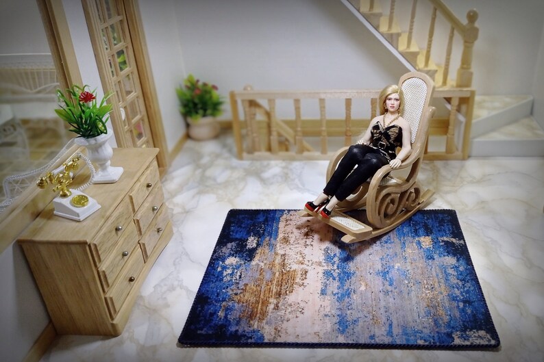 May include: Miniature dollhouse scene featuring a doll in a rocking chair on a blue, brown, and white rug. A wooden dresser, stairs, and a telephone are also visible. The rug has an abstract design.