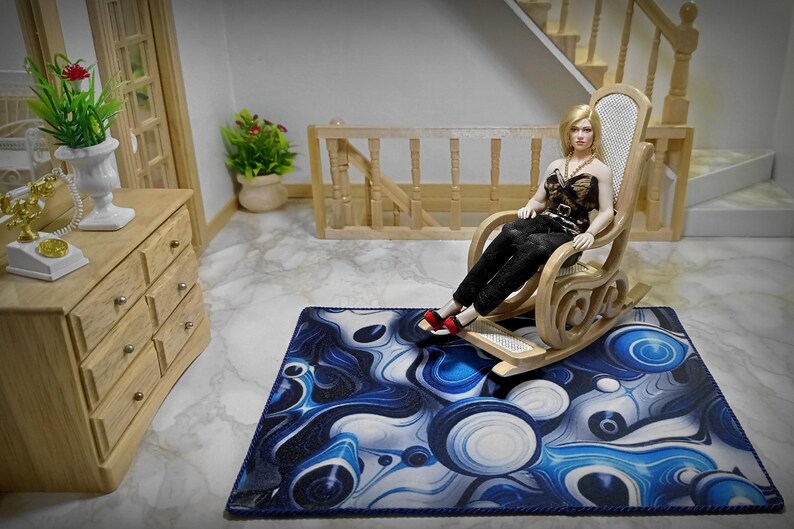 Peut inclure: Une poup&eacute;e miniature est assise dans un rocking-chair en bois sur un tapis &agrave; motifs bleus et blancs. La poup&eacute;e porte un pantalon noir et un haut &agrave; motifs. Une commode en bois et un t&eacute;l&eacute;phone sont visibles.