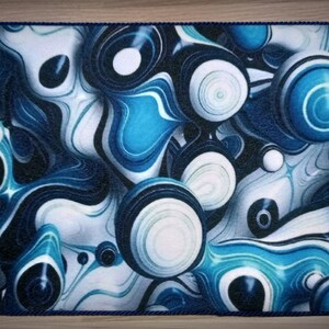 Peut inclure: Tapis rectangulaire avec un motif abstrait bleu et blanc pr&eacute;sentant des motifs tourbillonnants et des formes sph&eacute;riques. Le tapis a une bordure en corde bleu fonc&eacute; et le chiffre "3" dans le coin sup&eacute;rieur gauche.