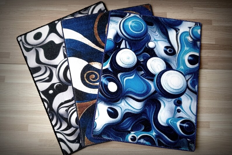 Peut inclure: Trois tapis d'art abstrait avec des motifs noirs, blancs, bleus et marron. Les tapis ont une bordure noire et sont dispos&eacute;s sur une surface en bois. Les motifs comprennent des motifs tourbillonnants et des formes sph&eacute;riques.