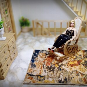 May include: Miniature dollhouse scene featuring a doll in a wooden rocking chair on a patterned rug. A wooden dresser with a white vase and a vintage telephone are also visible. The rug has a mix of colors.