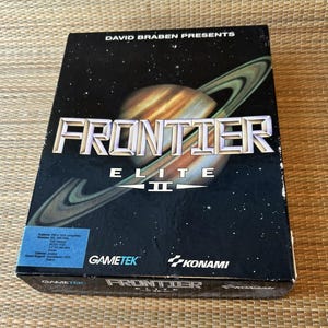 Puede incluir: Caja negra del juego "Frontier Elite II" con un diseño espacial. Muestra un planeta con anillos y el texto "David Braben Presents". También se ven los logotipos de Gametek y Konami.