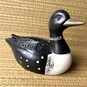 Könnte beinhalten: Dekorative Holzfigur einer Eistaucher-Ente. Der Vogel ist schwarz mit weißen Punkten und einer weißen Brust bemalt. Er hat einen silbernen Schnabel und rote Augen. Ein klassisches nordamerikanisches Wildtiersymbol.