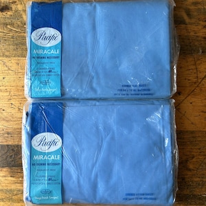 May include: Two packages of blue Pacific Miracale double flat sheets for a 137 x 198 cm mattress. The packaging states "no ironing necessary" and includes the text "a luxurious percale blend of 50% polyester 50% combed cotton."
