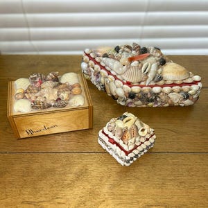 May include: Three decorative boxes adorned with various seashells. One rectangular wooden box features the word Aberdeen written in black ink. The other two boxes are entirely covered in a dense arrangement of assorted white, tan, and brown shells.