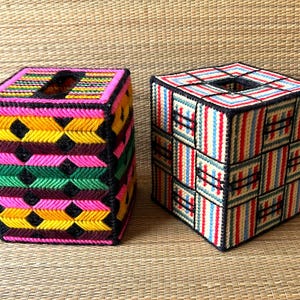 Könnte beinhalten: Zwei handgefertigte Taschentuchbox-Hüllen. Eine ist ein Würfel mit einem lebendigen Muster aus Pink, Gelb, Grün und Schwarz. Die andere ist ein Würfel mit rot, blau und weißen Streifen. Beide haben eine quadratische Öffnung oben.