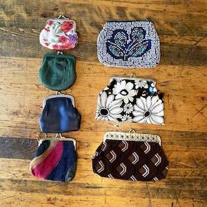 Può includere: Una collezione di portamonete vintage in vari stili e colori. Le borsette includono stampe floreali, disegni di perline e motivi geometrici. Le borsette sono realizzate con diversi materiali, tra cui tessuto e pelle.