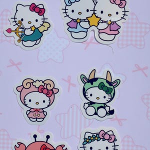 May include: Set of six Hello Kitty stickers featuring Hello Kitty dressed as different zodiac signs. The stickers are on a pink background with white stars.