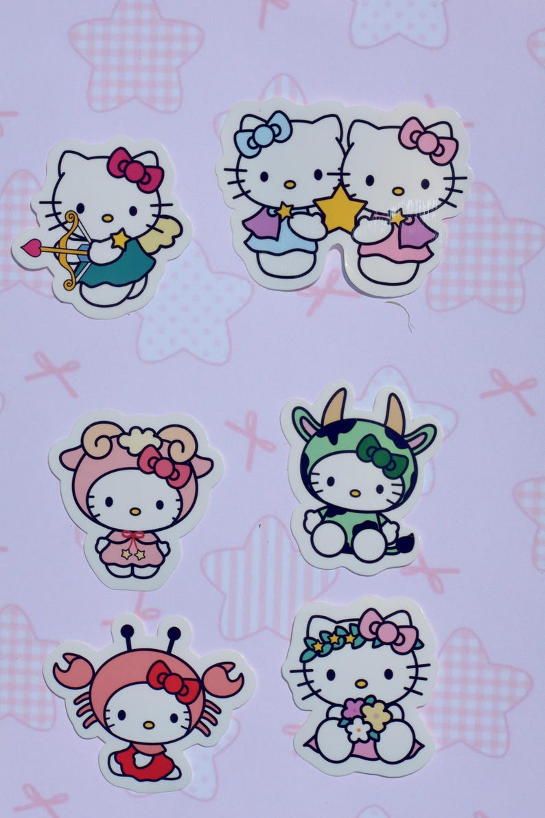 May include: Set of six Hello Kitty stickers featuring Hello Kitty dressed as different zodiac signs. The stickers are on a pink background with white stars.