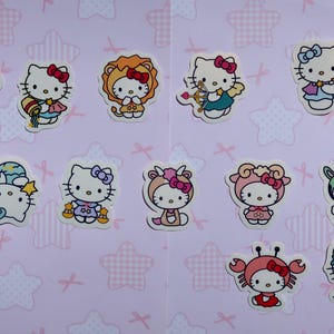 May include: A set of 12 Hello Kitty stickers featuring Hello Kitty dressed as different zodiac signs. The stickers are on a pink background with white stars and pink bows.