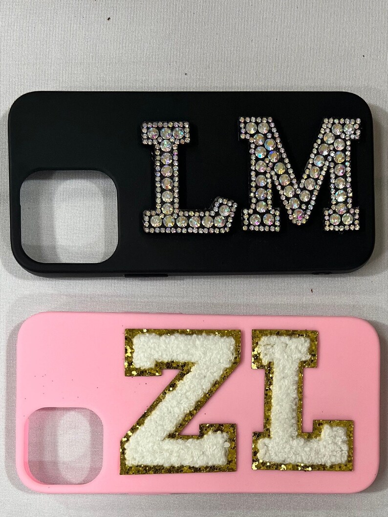 Może przedstawiać: Dwa etui na telefon z r&oacute;żnymi wzorami. Pierwsze etui jest czarne z literami "LM" w kryształach. Drugie etui jest r&oacute;żowe z literami "ZL" w kolorze białym z pozłacanymi obw&oacute;dkami.