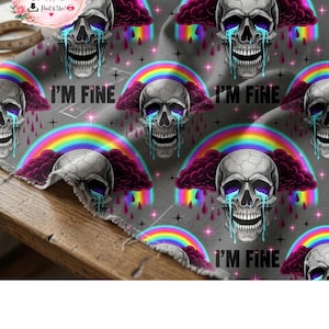 May include: Gray fabric with a repeating pattern of crying skulls, rainbows, and the text "I'M FINE." The skulls have purple clouds and tears. The rainbows are multi-colored. The fabric is draped over a wooden surface.