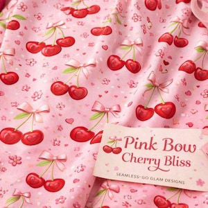 Puede incluir: Tela rosa con un estampado de cerezas rojas, tallos verdes y lazos rosas. La tela también tiene pequeñas flores y corazones. El texto "Pink Bow Cherry Bliss" está en una etiqueta.