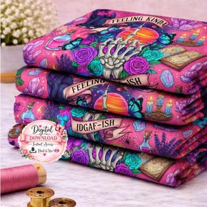 May include: A pile of pink fabric with a vibrant, fantastical design. The fabric features a skeleton hand, butterflies, roses, and crystals. The phrases "Feeling Kinda" and "IDGAF-ISH" are printed on the fabric.