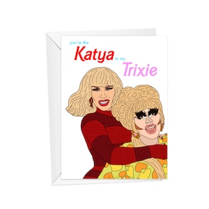 May include: A greeting card with a cartoon illustration of two drag queens, one with red hair and a red dress, and the other with blonde hair and a yellow and orange dress. The text on the card reads "You're the Katya to my Trixie."