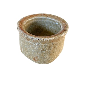 Puede incluir: Una pequeña maceta redonda de cerámica con un esmalte marrón claro y un borde marrón más oscuro. La maceta tiene una superficie rugosa y texturizada.