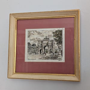May include: A framed black and white ink drawing of the Arc de Triomphe du Carrousel in Paris, featuring a dusty rose mount and a light cream-coloured wooden frame with gold inner trim. The artwork includes the text Arc de Triomphe du Carrousel.