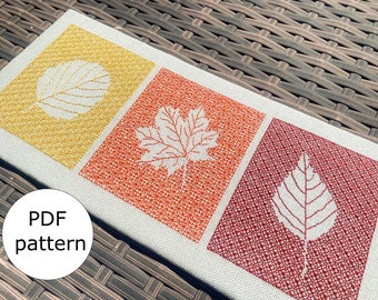 May include: A white canvas with three embroidered leaf designs. The leaves are outlined in white and the background is filled with a pattern of small stitches. The background colors are yellow, orange, and red.